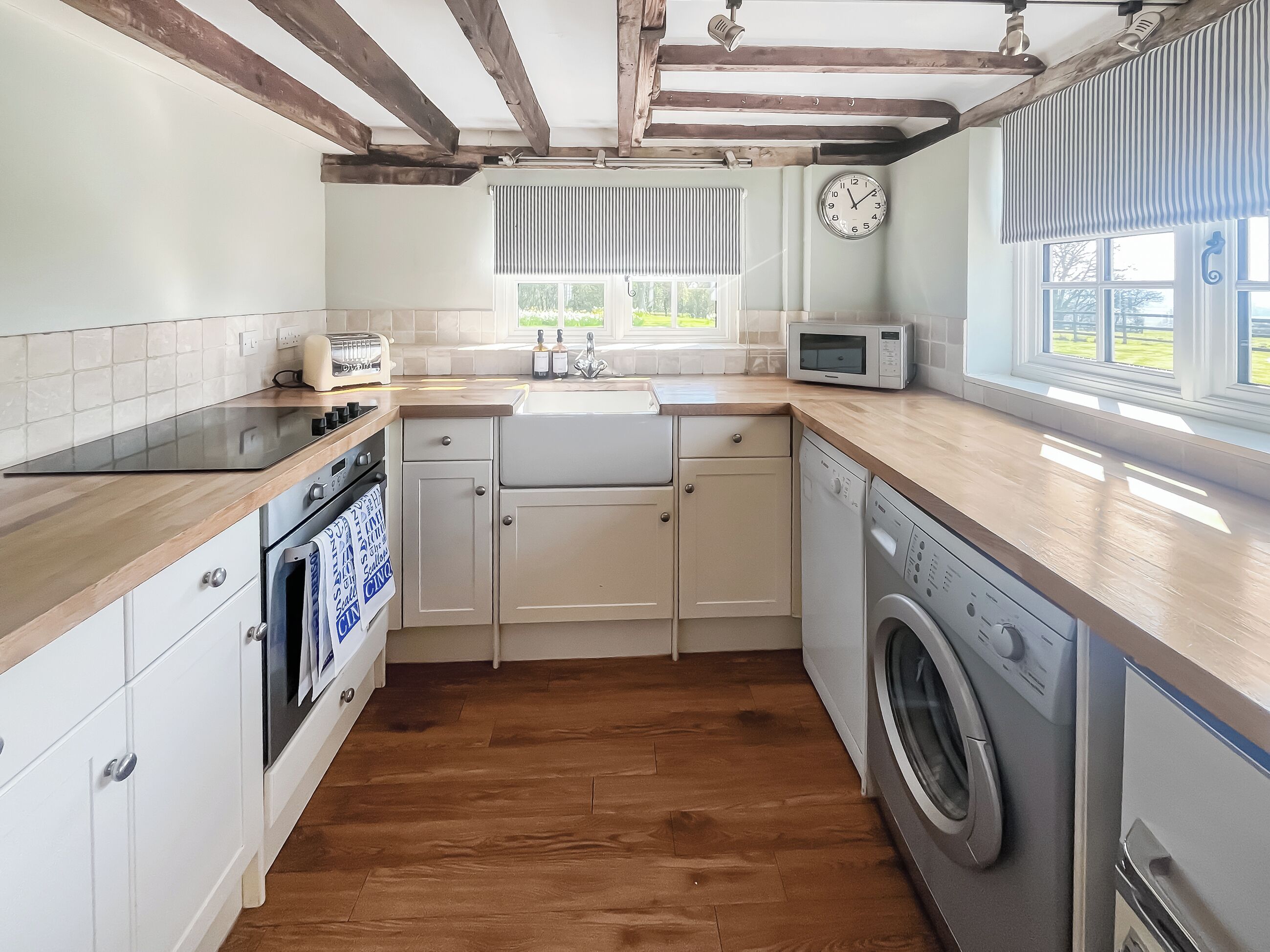 A kitchen with wooden beams, a microwave, a washing machine, and a clock.