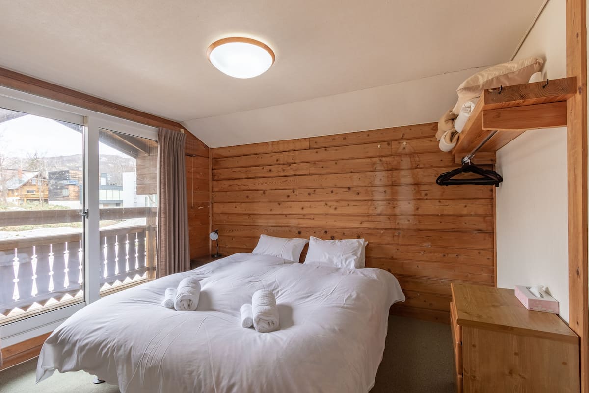 Una habitación con paneles de madera, una cama, un tocador de madera y una ventana con cortinas.