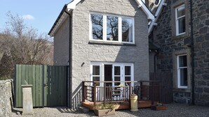 A two-story stone house with a balcony, a green gate, and a small garden area. - 1 bedroom accommodation in St Fillans, near Crieff (St Fillans, near Crieff)