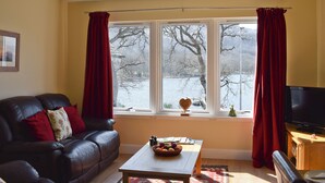A living room with a leather sofa, a wooden coffee table with a fruit bowl, a television, and a window with curtains. - 1 bedroom accommodation in St Fillans, near Crieff (St Fillans, near Crieff)