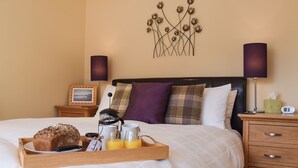 A neatly made bed with a tray of breakfast items, a bedside table with a lamp, a clock, and a decorative wall piece. - 1 bedroom accommodation in St Fillans, near Crieff (St Fillans, near Crieff)