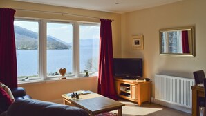 A living room with a large window, a television, and a radiator. - 1 bedroom accommodation in St Fillans, near Crieff (St Fillans, near Crieff)
