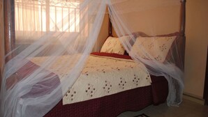 Una cama con dosel, una colcha estampada y una almohada roja decorativa.