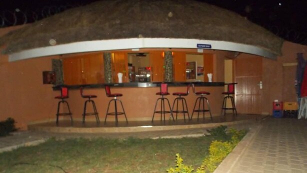 Zona de bar con taburetes y una barra, rodeada por un muro bajo y una zona verde con flores amarillas.