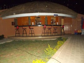 Zona de bar con taburetes y una barra, rodeada por un muro bajo y una zona verde con flores amarillas.