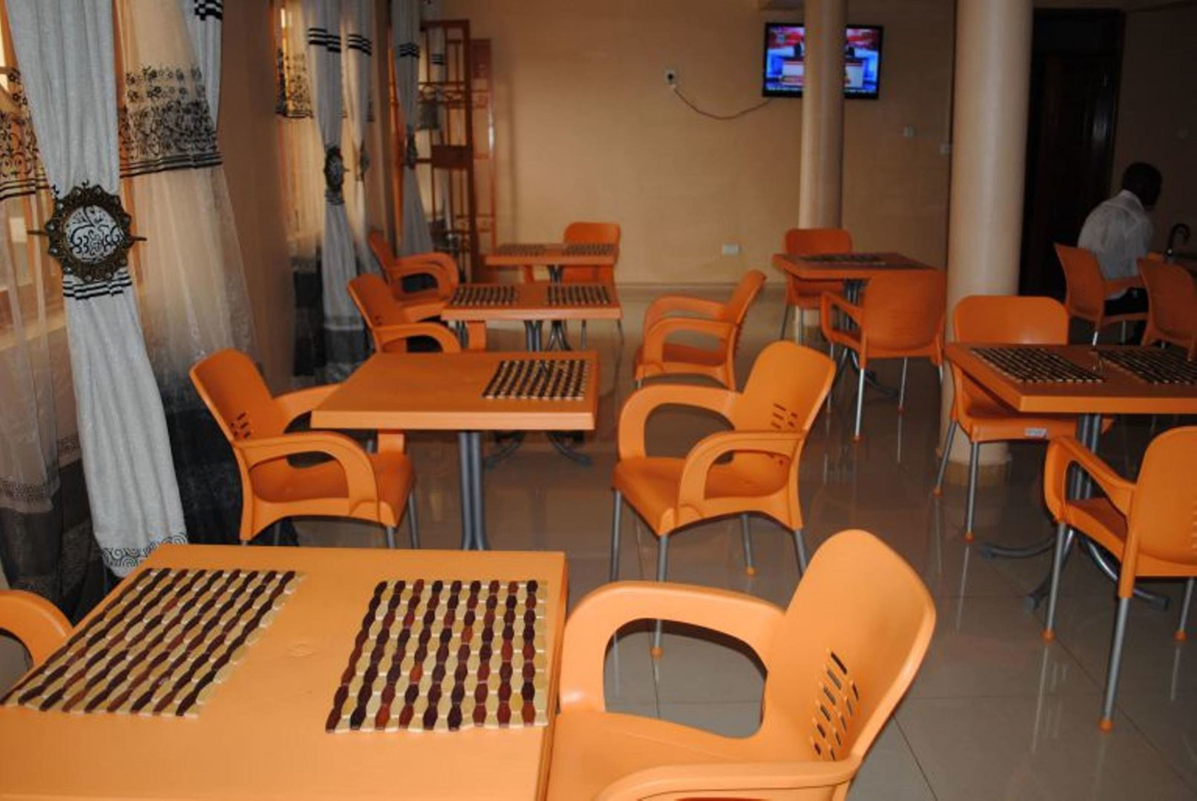 A dining area with orange chairs and tables, some with chessboards on them.