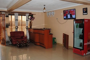 Una sala de estar con un mostrador de recepción de madera, un sofá rojo, un taburete verde, un televisor montado en la pared y un refrigerador rojo Coca-Cola.