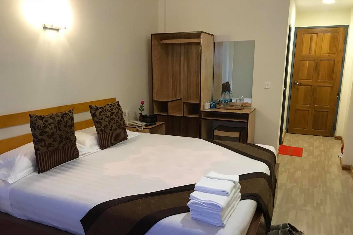 Quarto de hotel com cama grande, guarda-roupa de madeira, escrivaninha com espelho e uma porta.