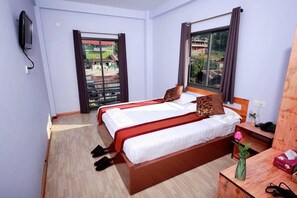 Ein Hotelzimmer mit einem großen Bett, einem Holzkopfende, einem kleinen Nachttisch, einem an der Wand montierten Fernseher und einem Fenster mit Vorhängen.