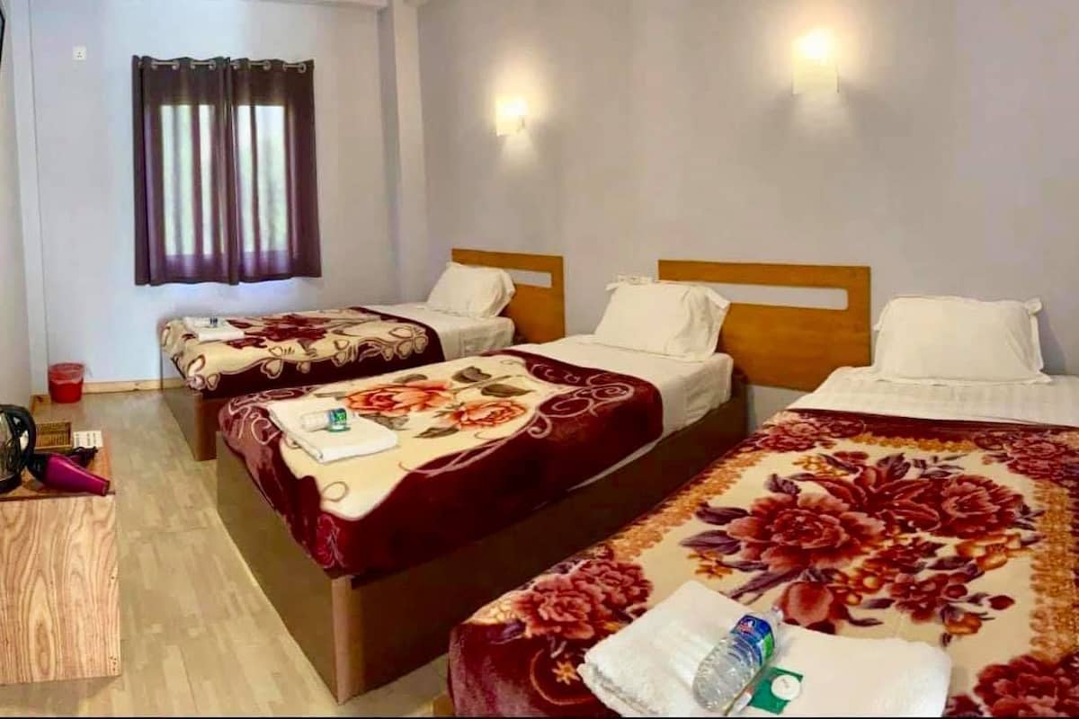 Quarto de hotel com três camas de solteiro, cada uma com colcha florida, cabeceira de madeira e luminária fixada na parede.