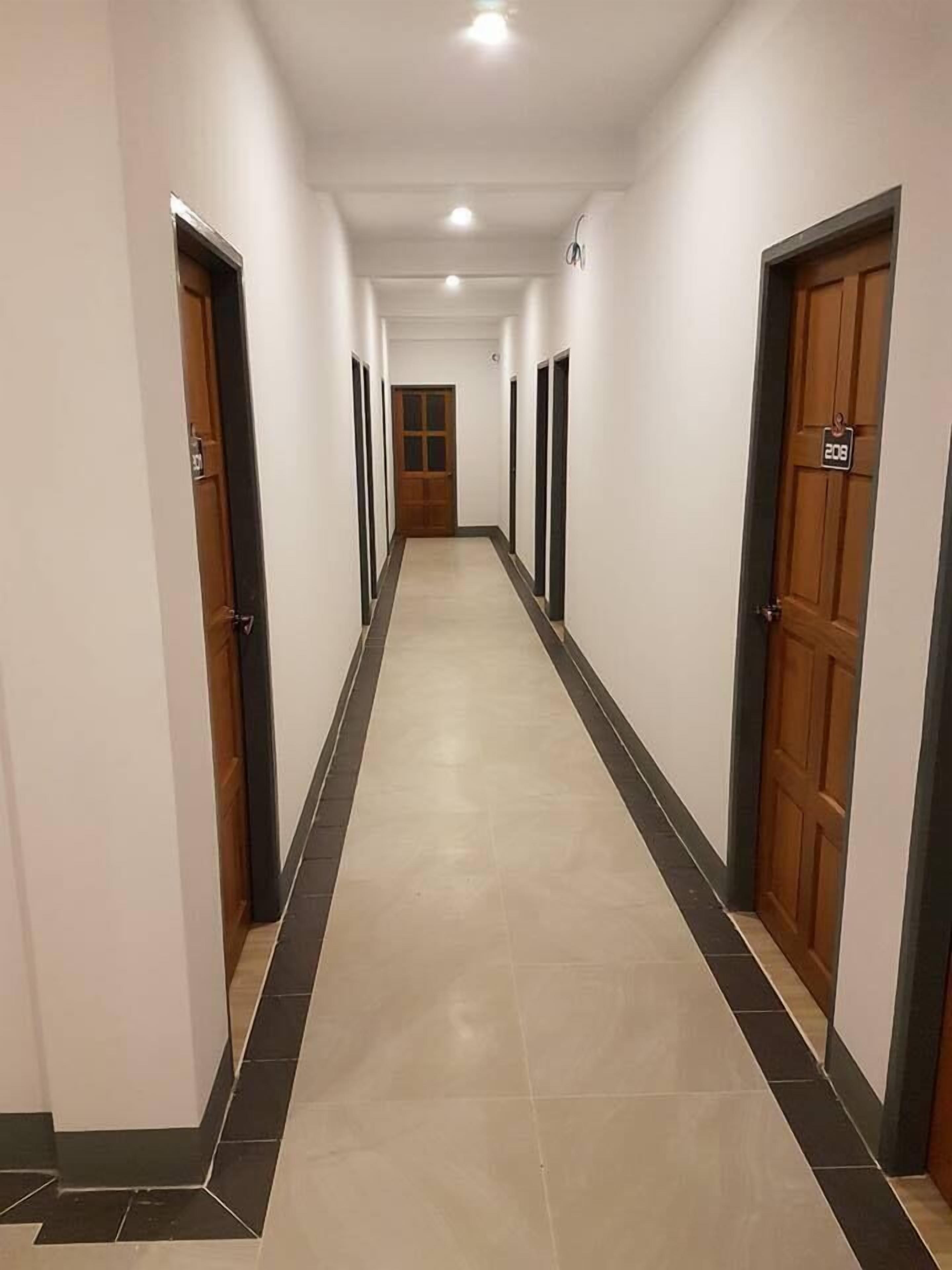 A long, narrow hallway with white walls, wooden doors, and a tiled floor.