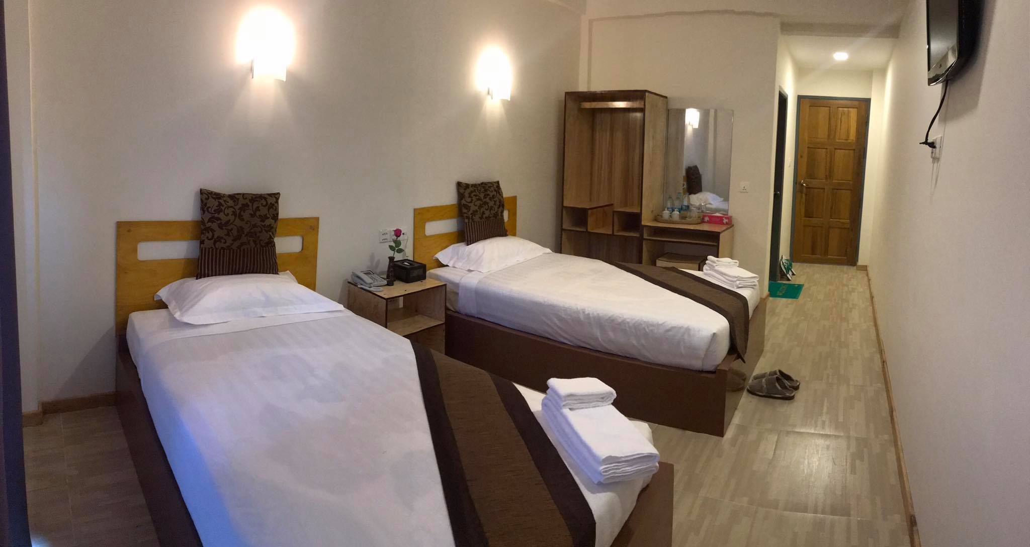 Habitación de hotel con dos camas, un armario, un espejo y un televisor montado en la pared.