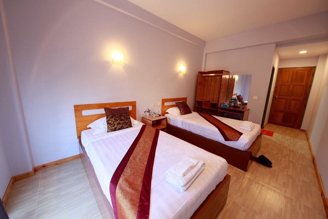 Une chambre d’hôtel avec deux lits simples, une armoire en bois, une table de chevet avec une lampe et un miroir.