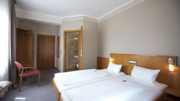 A hotel room with two beds, a shower, a wooden headboard, a bedside table, and a chair.
