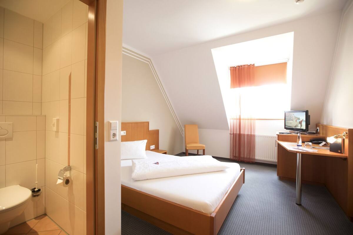A hotel room with a bed, a desk, a television, and a window with curtains.