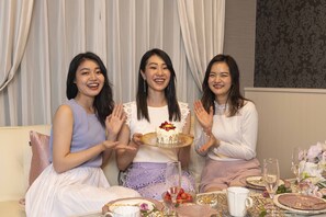 Three people seated at a table with a cake, surrounded by floral decorations and a patterned wall. - Framboise KYOTO Hotel de charme (Kyoto)