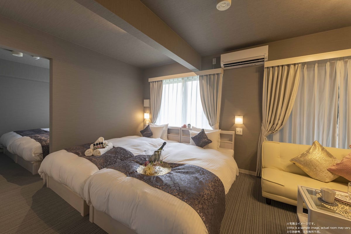 A hotel room with two beds, a sofa, a small table, and a window with curtains.