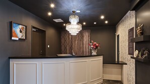 A modern reception area with a curved white counter, a chandelier, a framed artwork, and a floral arrangement. - Framboise KYOTO Hotel de charme (Kyoto)