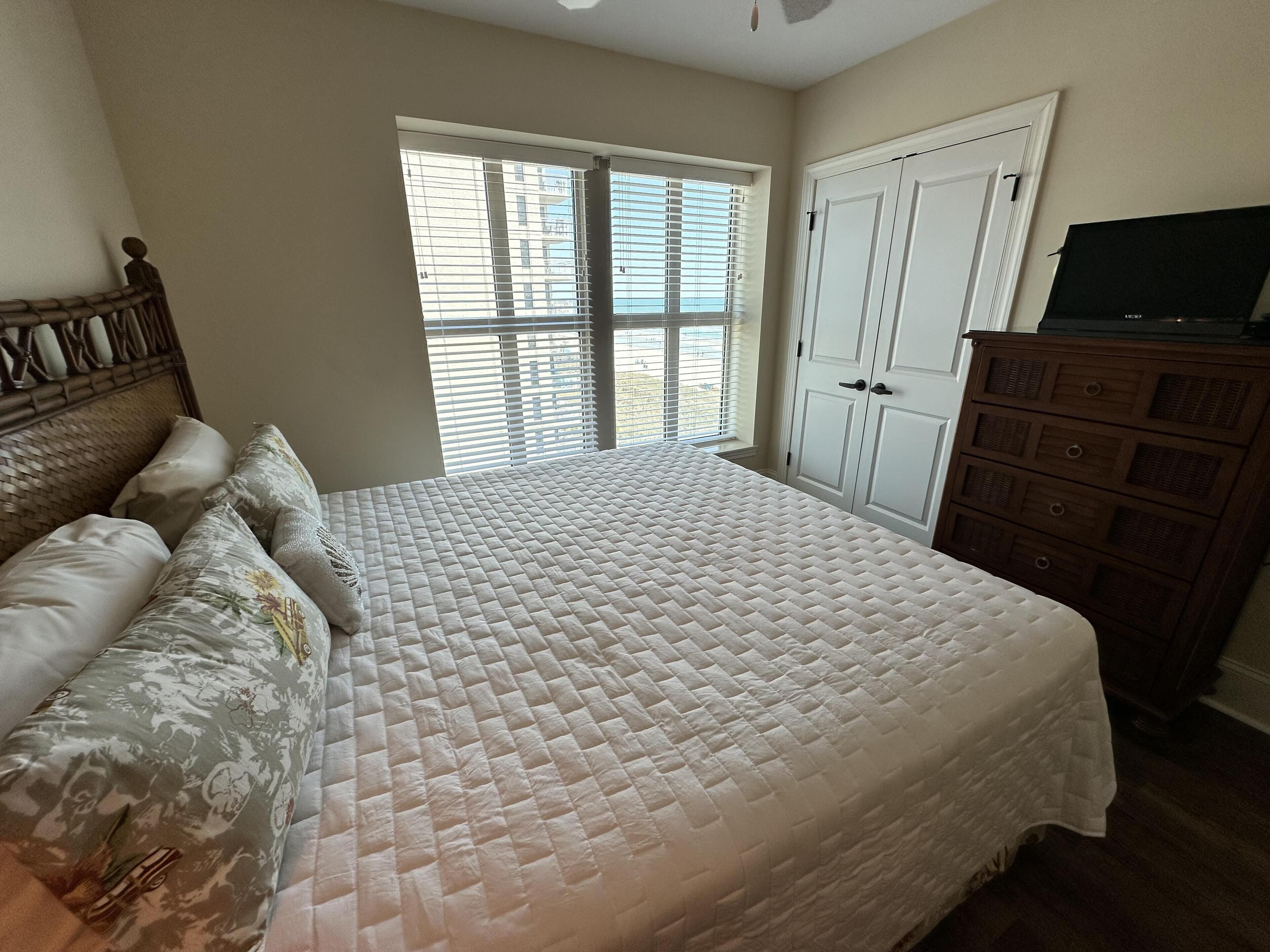 A bedroom with a bed, a dresser, and a window with blinds.