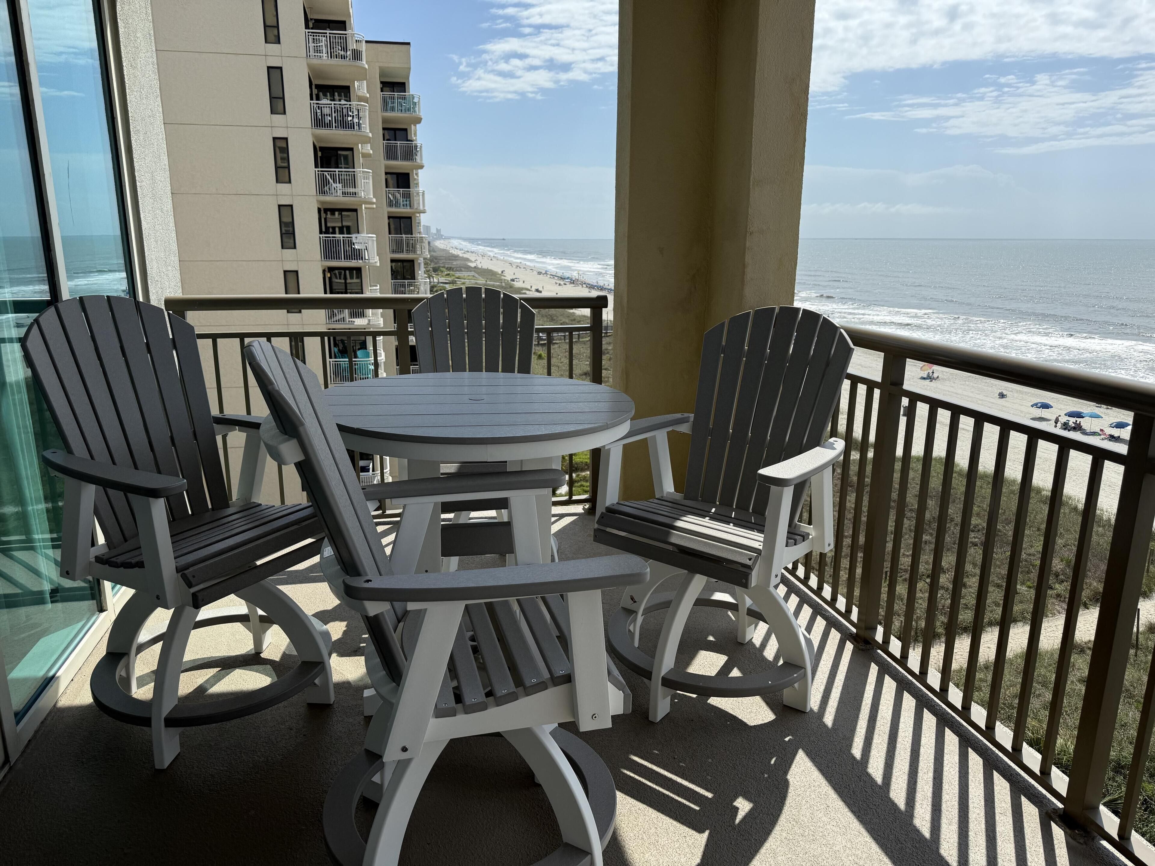 Een balkon met Adirondack-stoelen en een tafel, met uitzicht op een strand en de oceaan.