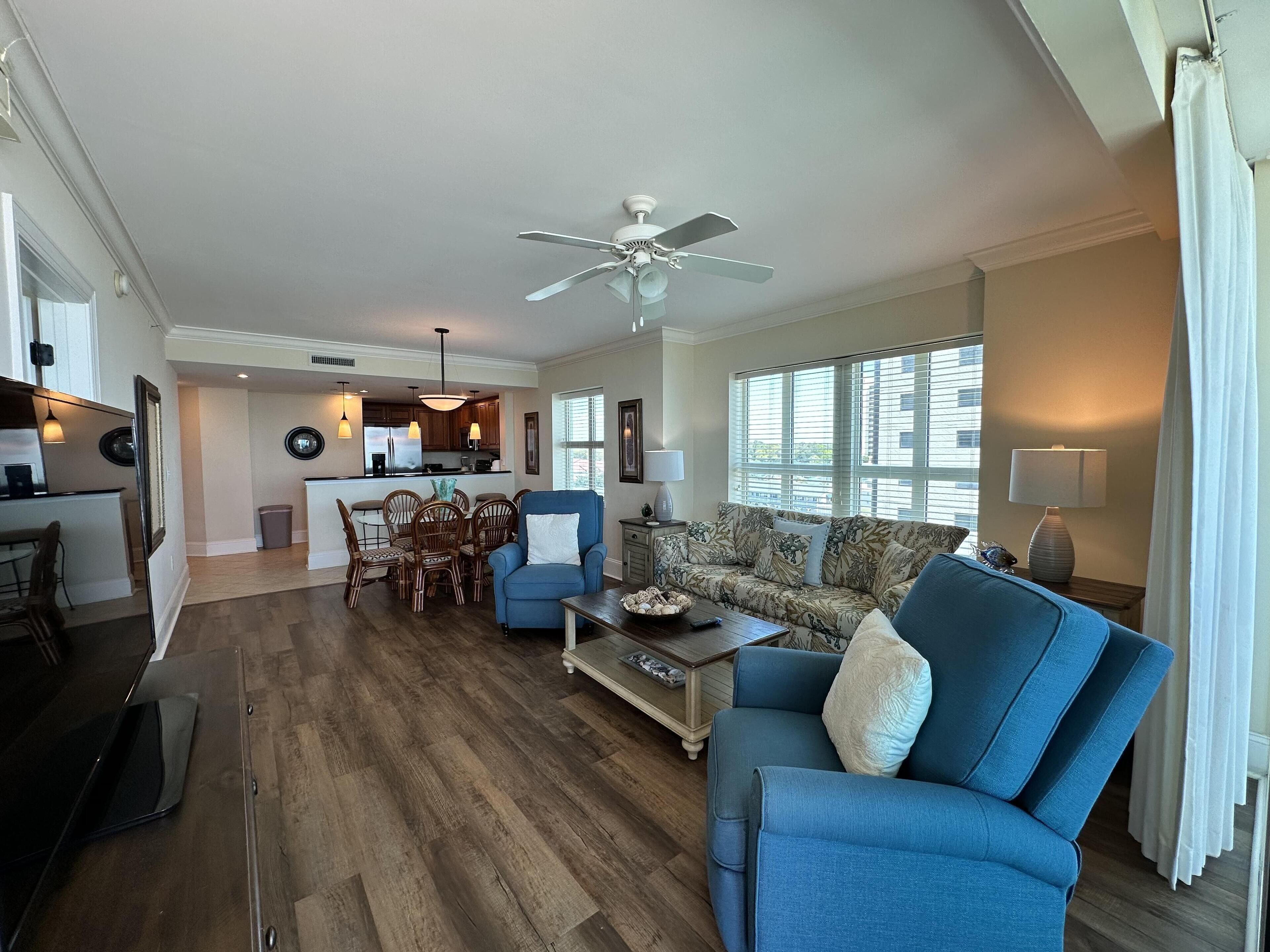 A spacious living room with a blue armchair, a sofa, and a dining area with wooden chairs and a table.