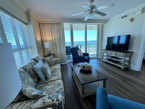 Relax in this stylish living room with a large TV, comfortable armchair, and sofa, offering a view of the ocean.