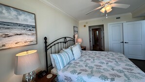 Ein Schlafzimmer mit einem Bett, einem Deckenventilator, einem Nachttisch mit Lampe und einer Tür zu einem anderen Raum.