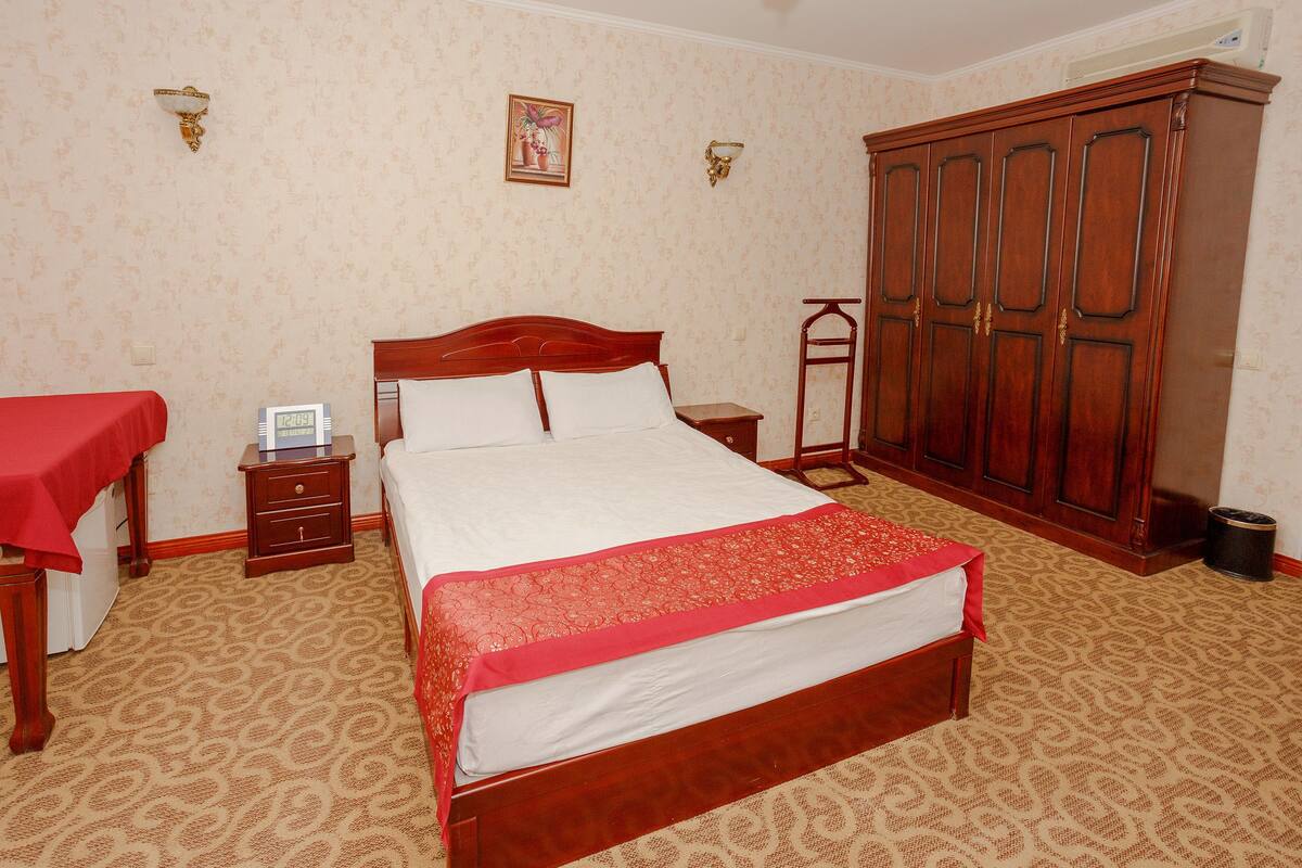 A bedroom with a wooden bed, a nightstand, a wardrobe, and a red tablecloth on the bed.