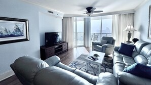 Een moderne woonkamer met een flatscreen televisie, leren banken, een salontafel en een plafondventilator.