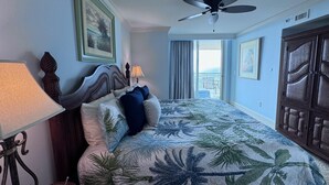 Hotelkamer met een bed, een plafondventilator, een nachtkastje met lamp en uitzicht op het balkon.