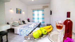 Una camera d'albergo con un letto, un tavolo con frutta e una bottiglia, e una finestra con tende.