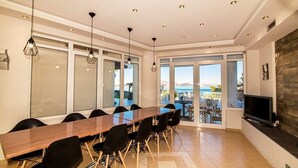 Un'area pranzo moderna con un lungo tavolo in legno e sedie nere, ampie finestre con vista e un televisore a schermo piatto su un supporto nero.