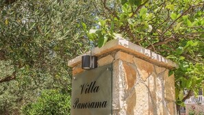 Un cartello in pietra con la scritta "Villa Panorama", circondato da ulivi.