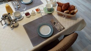 A breakfast setting with a table set for two, including plates, cutlery, a teapot, cups, a glass of orange juice, croissants, and bread. - Le Coze (Saint-Martial-de-Nabirat)