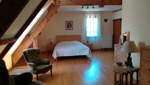 A bedroom with a wooden floor, a bed, a chair, a dresser, and a window with curtains. - Le Coze (Saint-Martial-de-Nabirat)