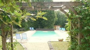A wooden pergola over a swimming pool with lounge chairs and a garden area. - Le Coze (Saint-Martial-de-Nabirat)