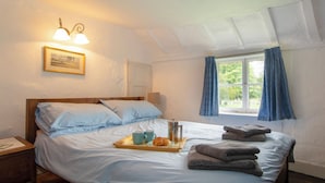 Une chambre à coucher avec un lit en bois, une table de chevet, une fenêtre avec des rideaux et un luminaire fixé au mur.