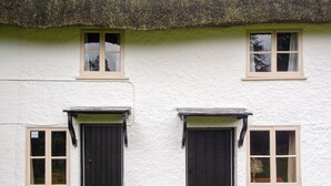 Un bâtiment blanc avec deux portes et fenêtres noires, un toit de chaume et un petit jardin.