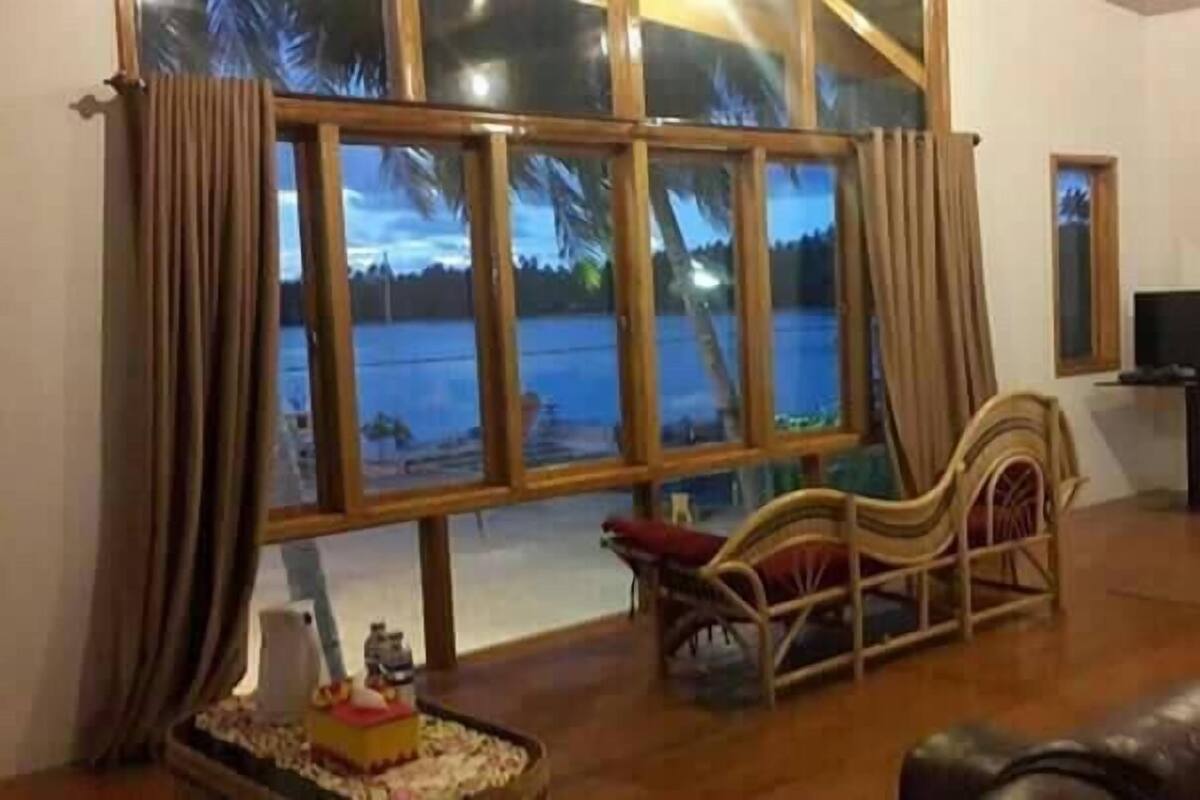A spacious living room with a large window offering a view of a body of water. There is a wooden chair and a small table with a decorative item.
