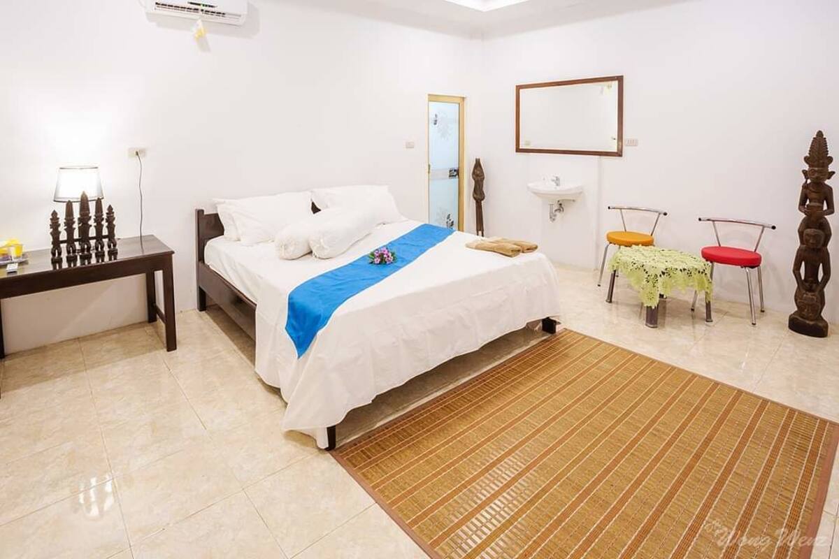 A hotel room with a bed, bedside table, lamp, mirror, and a small statue.