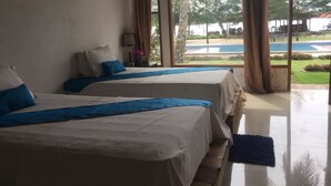 Habitación de hotel con dos camas, un ventanal con vistas a una piscina y zonas verdes, y suelo de madera.