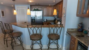 A kitchen with a central island, bar stools, a refrigerator, and wooden cabinets. - MVG 1510 Oceanfront, Penthouse (North Myrtle Beach)