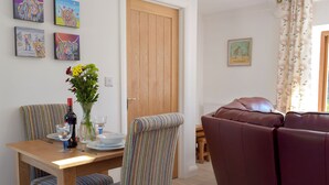A dining area with a wooden table, striped chairs, and a vase of flowers. There is a brown leather sofa and a wooden door in the background. - Hen Llaeth - UK11209 (Cwmsychpant, near Lampeter)