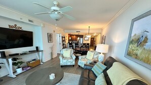 A living room with a TV, a ceiling fan, a sofa, armchairs, a coffee table, and a painting on the wall. - MVG 511 3 bedroom 3 bath Oceanfront (North Myrtle Beach)
