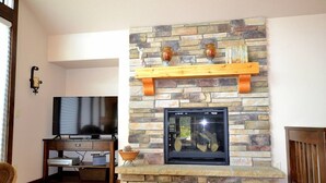 A living room with a stone fireplace, wooden shelves, a flat-screen TV, and a wooden coffee table. - The Summit - 3 bedroom 2.5 bathroom home - walk to town (Estes Park)
