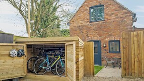 A wooden bike shed with two bicycles inside, a brick house with a window, and a tree in the background. - 1 bedroom accommodation in Wainfleet, near Skegness (Wainfleet, near Skegness)