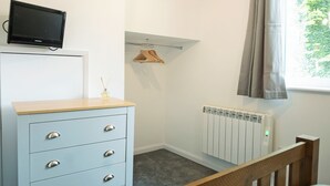 A room with a blue dresser, a television on top, a radiator, a wooden chair, and a window with curtains. - 1 bedroom accommodation in Wainfleet, near Skegness (Wainfleet, near Skegness)