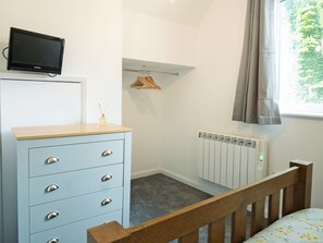 A room with a blue dresser, a television on top, a radiator, a wooden chair, and a window with curtains. - 1 bedroom accommodation in Wainfleet, near Skegness (Wainfleet, near Skegness)