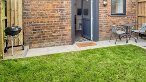 A brick house with a dark door, a barbecue grill, and a small outdoor seating area with two chairs and a table. - 1 bedroom accommodation in Wainfleet, near Skegness (Wainfleet, near Skegness)