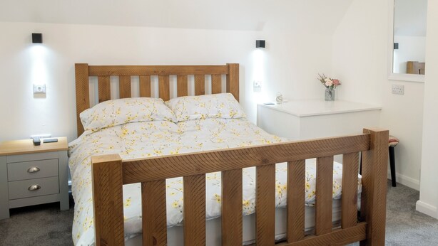 A bedroom with a wooden bed, a bedside table, a nightstand, a small desk, and a mirror on the wall. - 1 bedroom accommodation in Wainfleet, near Skegness (Wainfleet, near Skegness)